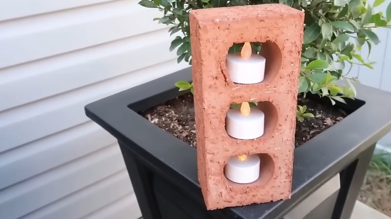perforated brick with battery powered tealight candles in the holes, sitting on the edge of an outdoor potted plant