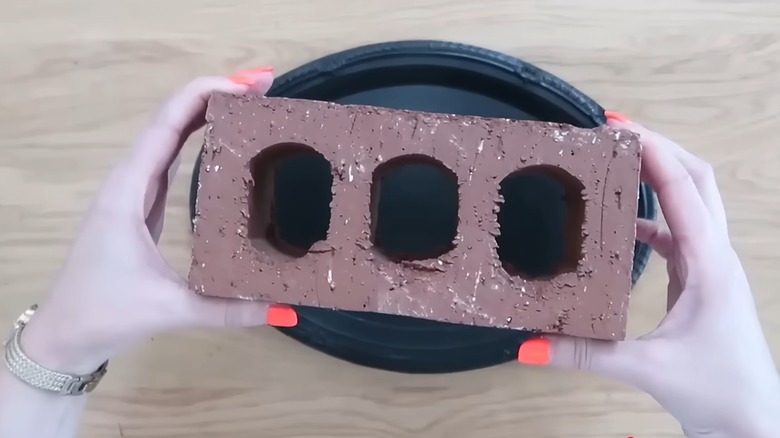 A woman with painted nails prepares a brick for a DIY project