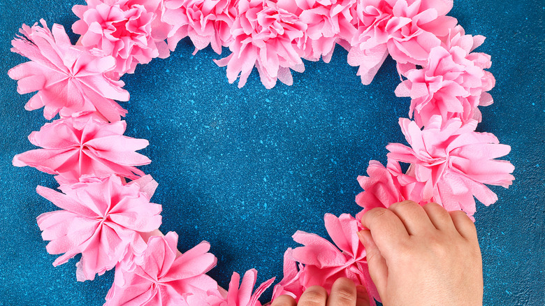 Hands adding pink paper flowers to a heart-shaped wreath