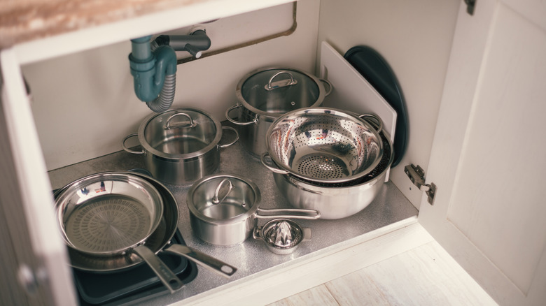 pots and kitchen gear sitting under the kitchen sink in a cabinet
