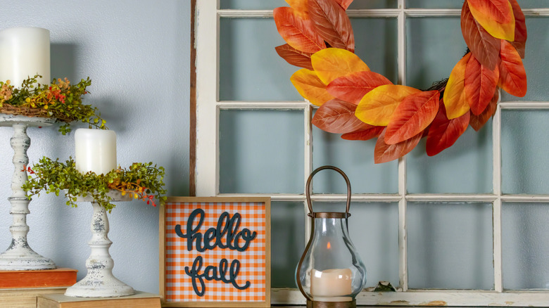 An autumn wreath hanging from an old window propped against a wall.