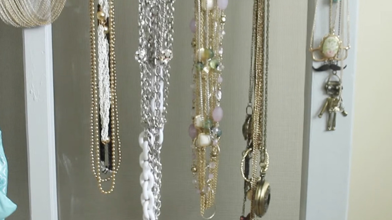 A window with a screen being used to hold jewelry.