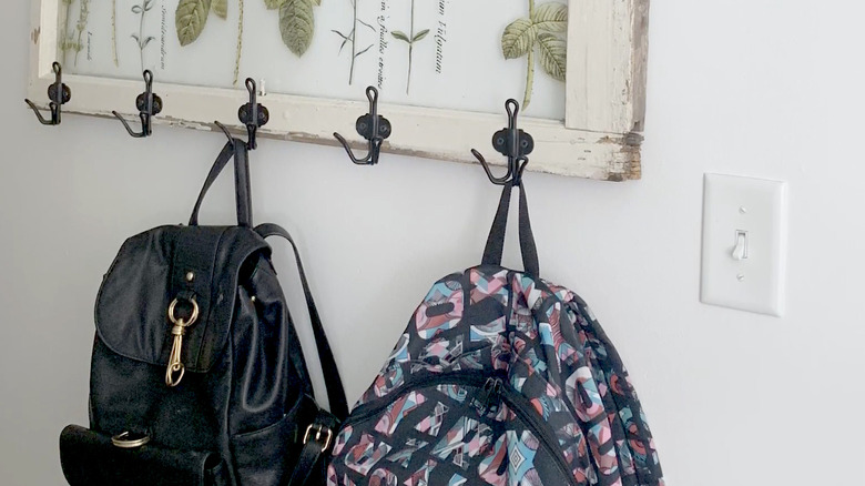 A salvaged old window with hooks attached holding backpacks.