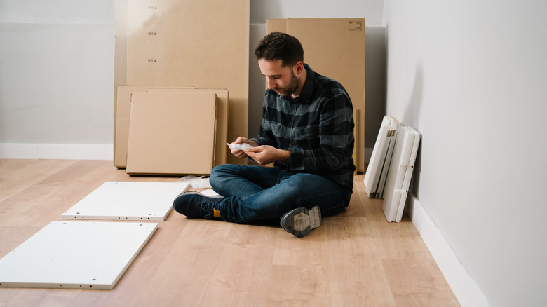 Man sitting on the ground as he puts together an IKEA furniture piece.