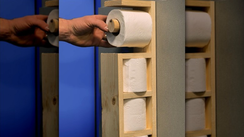 Person putting roll on DIY wall-mounted toilet paper holder made from scrap wood