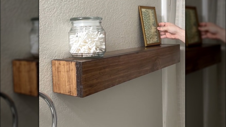 Woman setting up DIY wooden wall shelf with glass cannister and picture frame in bathroom