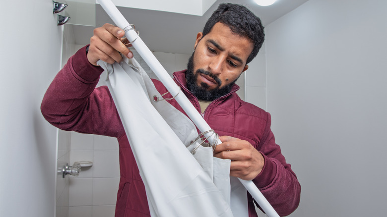 A man removes his shower curtain roll, with rings attached