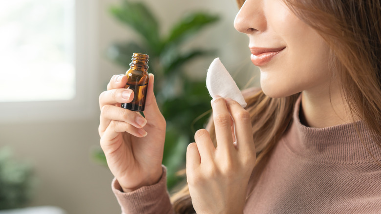 Woman wearing a sweater holding a bottle of clove essential oil and a cotton swab
