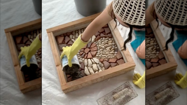 A woman kneels while pouring mortar over a DIY stone paver design