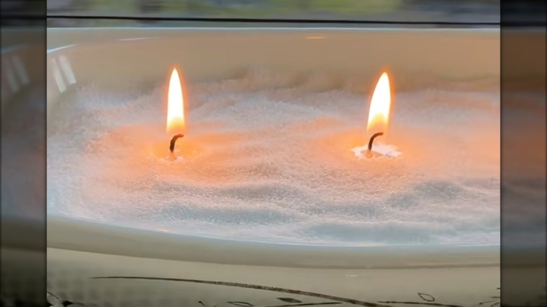 Close up of a thrifted Pyrex casserole dish with Vogue Candle wax beads and two lit wicks