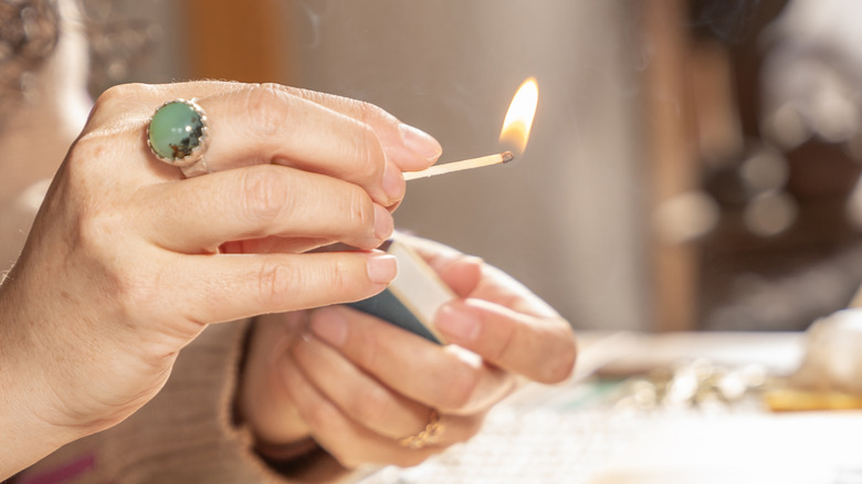 A woman lights a match in a softly lit room