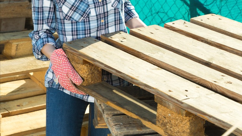 Person wearing gloves pulling old wood pallet off of a stack