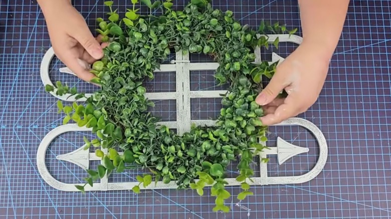 A person places a faux boxwood wreath on top of two white Dollar Tree garden fence panels