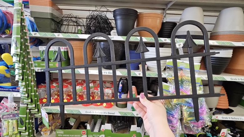 A person holds up a piece of black decorative fencing in front of stocked shelves at Dollar Tree
