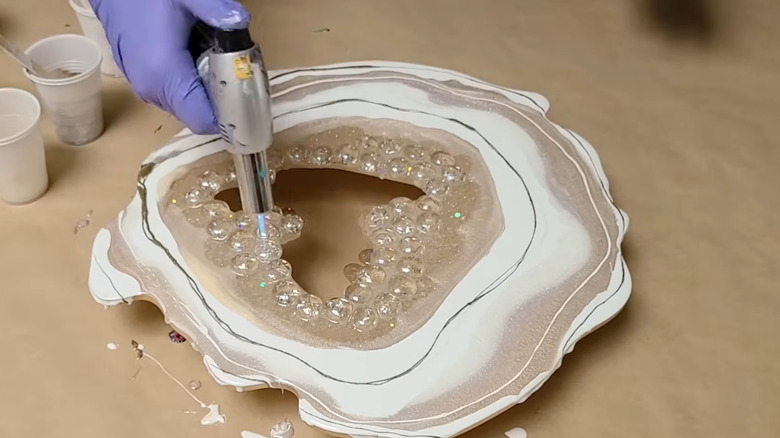 a person uses a small blowtorch to release air bubbles from a resin geode