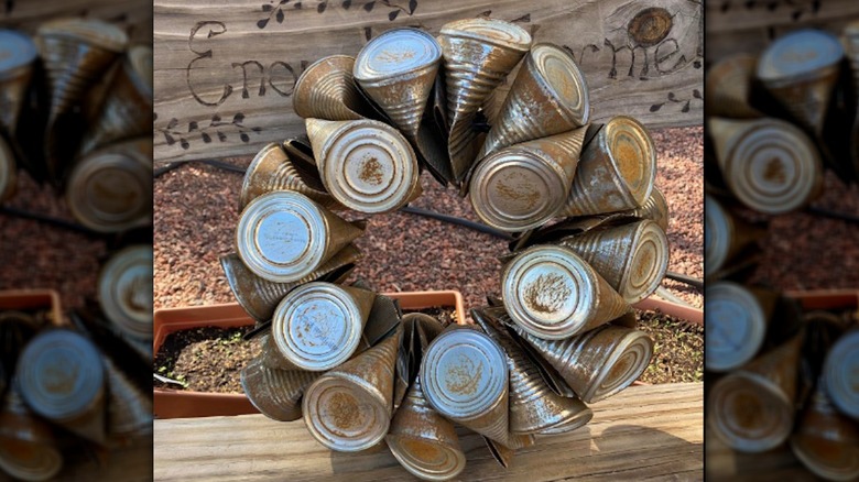 Wreath made of rusted tin cans on wooden bench.