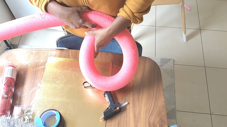 Young woman curving pink foam pool noodle for DIY project over wood table with supplies