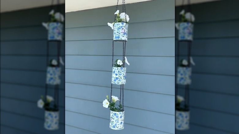 Decoupaged tin cans with light blue floral design and white flowers hanging beside blue house siding
