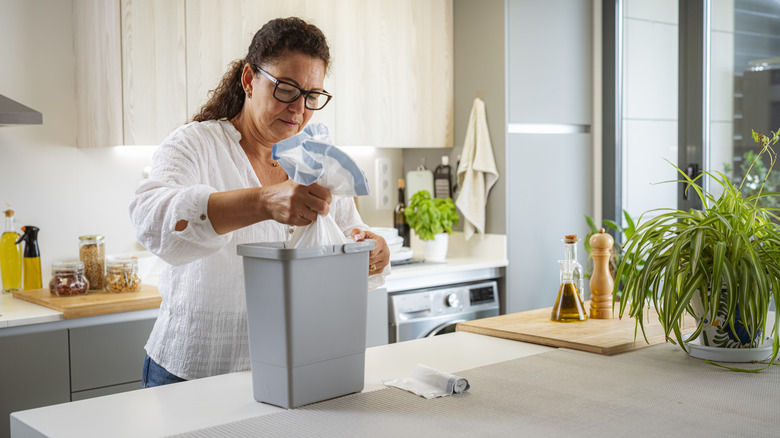A woman empties a small kitchen trash can