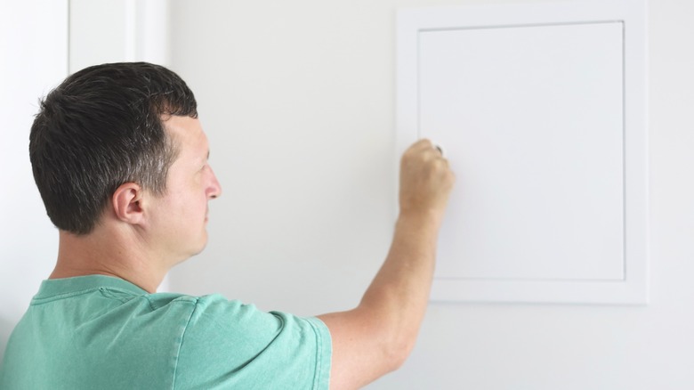 Man opening breaker box door on wall