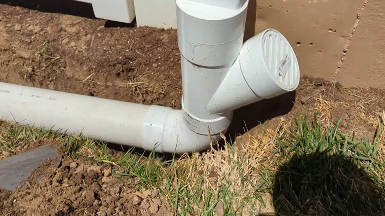 A downspout attached to a PVC pipe that's sitting in a trench, about to be covered