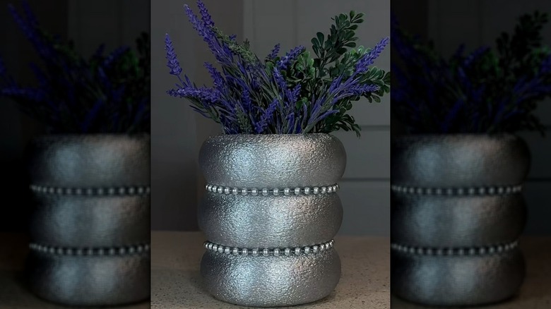 A silver-colored stacked vase with flowers in it