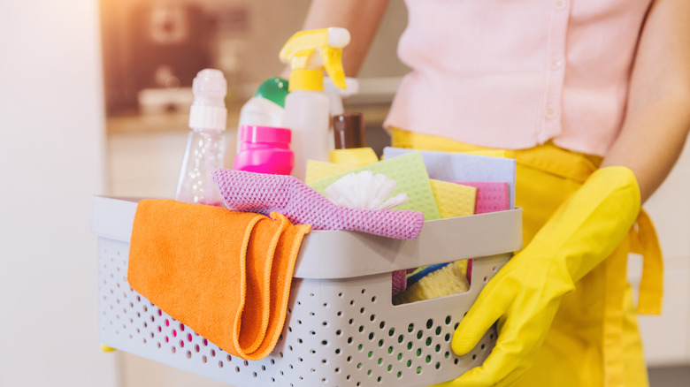 Person holding various laundry and cleaning supplies in a basket