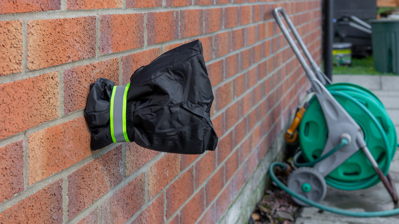 Outdoor faucet on a brick wall covered with an insulated black bag.