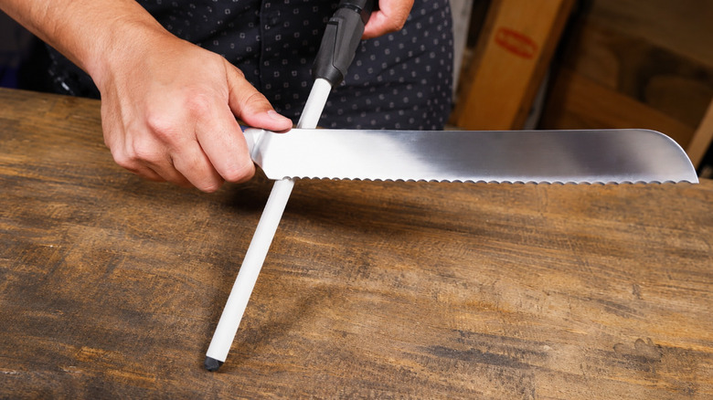 A man a sharpening rod on a serrated blade