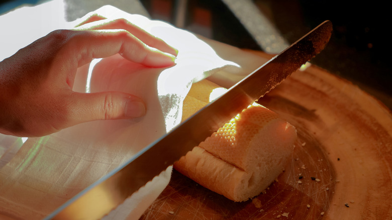 A serrated knife being used to cut a baguette