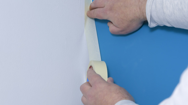 Hands applying white painter's tape to a painted wall