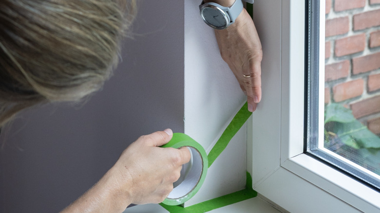 Woman adding green painter's tape along a window's egdes