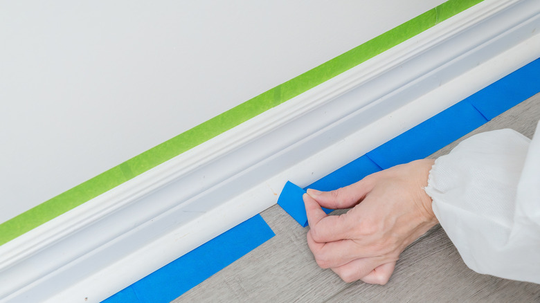 Hands adding blue and green painter's tape to a baseboard