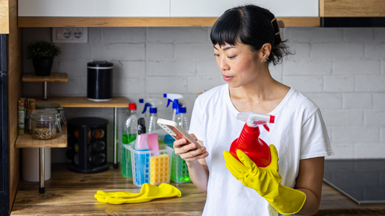 Person looking at smartphone while holding a red spray bottle