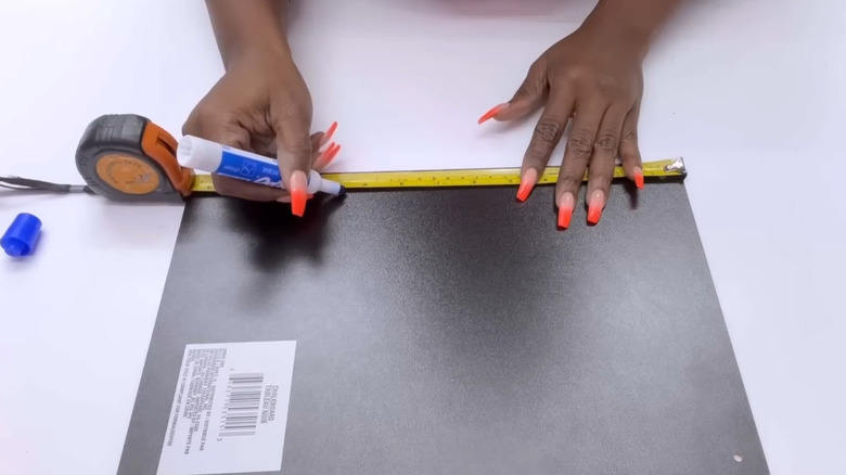 A woman with long colorful nails measures a Dollar Tree chalk board