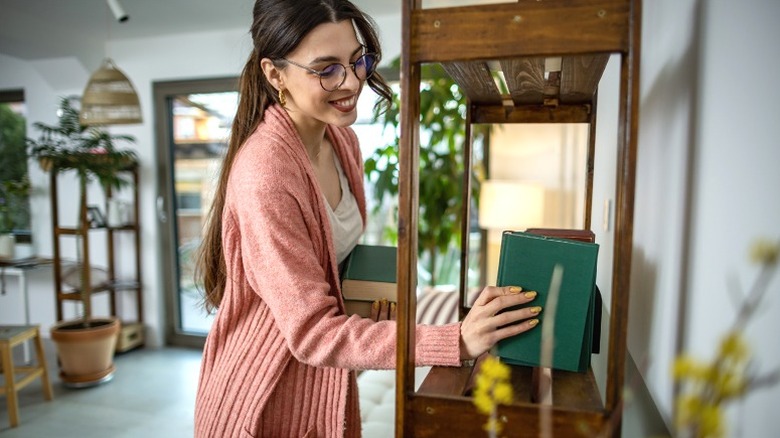 Pretty woman organizing books on shelf at home