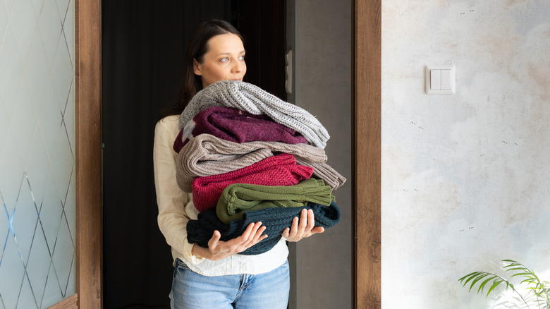 A woman stands in a doorway holding a large stack of colorful blankets