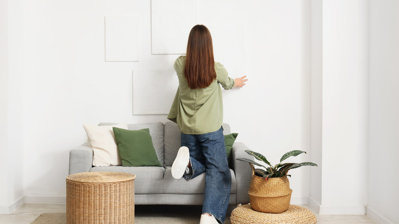 Woman hanging wall decor on blank white wall