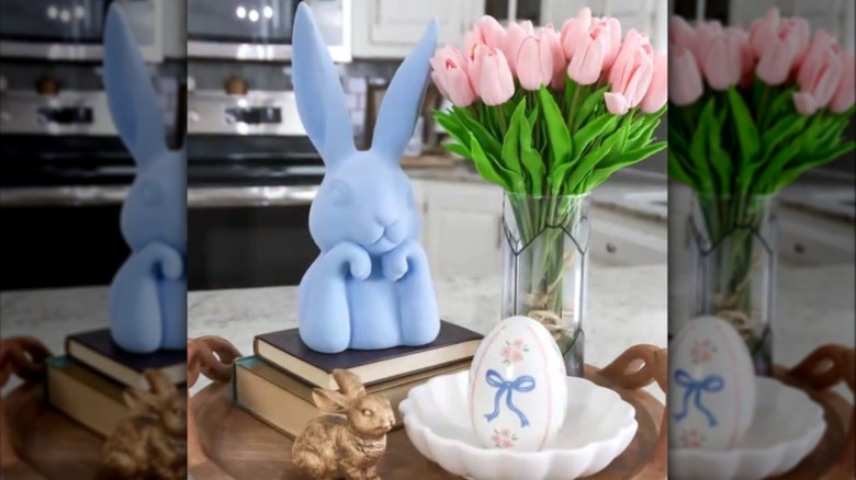 A Dollar Tree vase wrapped in cling film resting next to bunny decor on a kitchen counter.