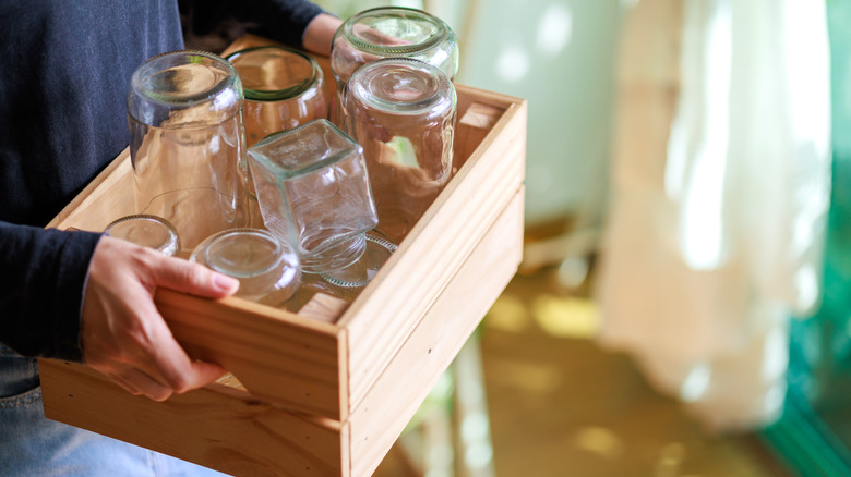 Person carrying empty mason jars in a wooden box