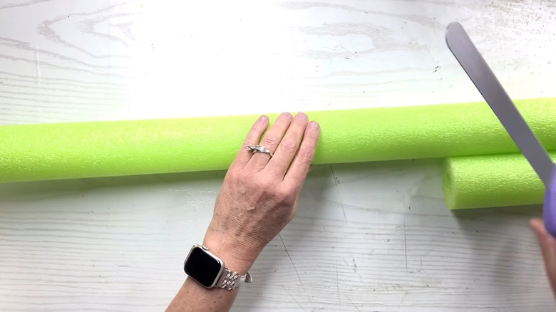 Person cutting a neon green pool noodle on a wooden table
