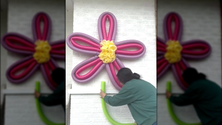 Woman shaping multiple pool noodles into outdoor flower sculpture for garden