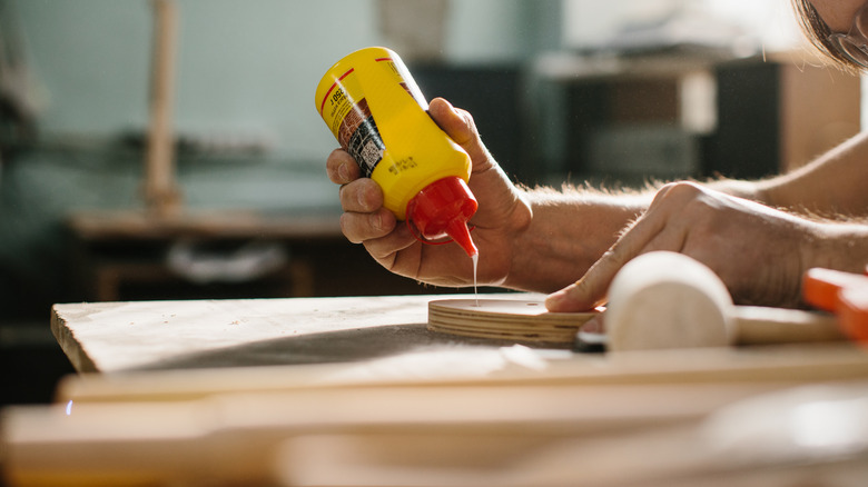 Someone applying glue from a yellow bottle to a piece of wood