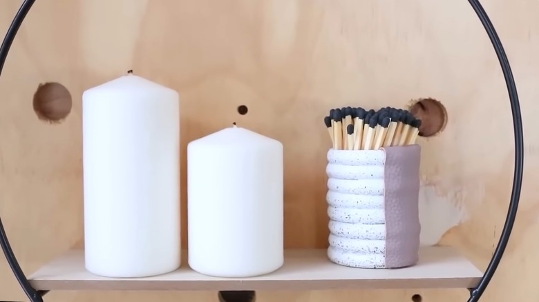 Matchsticks in DIY shower ring holder with leather strip beside white candles on contemporary wall shelf