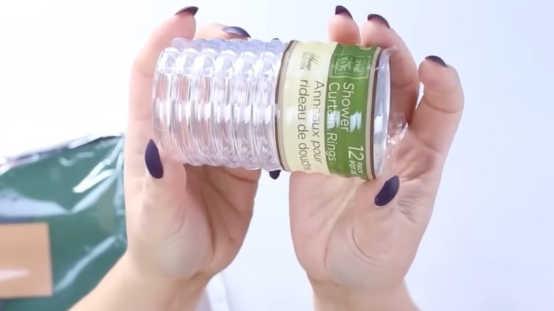 Woman with manicured nails holding up pack of Dollar Tree shower rings for DIY project