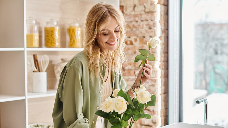 A woman smiles and arranges flowers in a kitchen