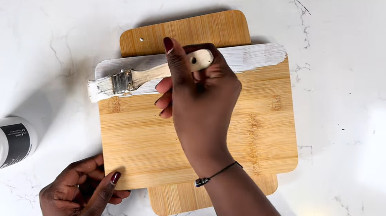 Hands painting a wooden cutting board from Dollar Tree