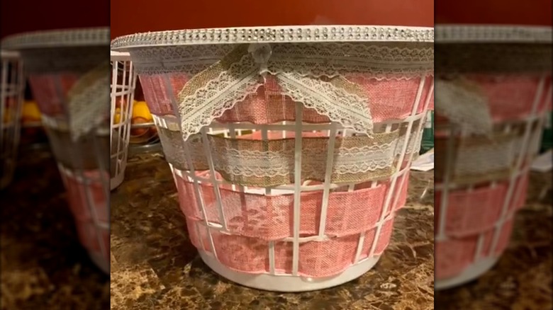 Brown and pink lacey burlap woven between plastic slats of dollar store laundry hamper for pillow storage