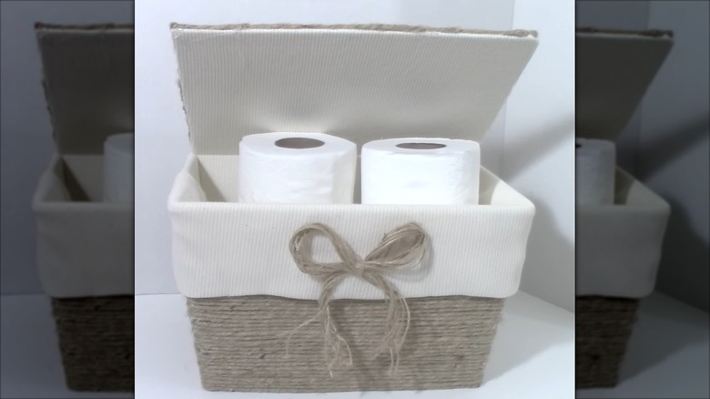 Rustic twine and fabric-lined basket with toilet paper rolls on white surface