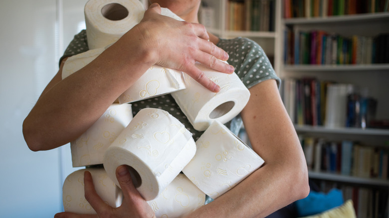 Young woman carrying multiple toilet paper rolls at home